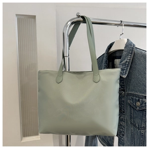 Detail of mint green nylon tote bag hanging on rack with denim jacket background