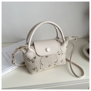 Close-up of woven mini crossbody bag featuring floral embroidery and white leather details