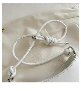 Detailed close-up of a white leather handbag featuring a knotted strap and silver hardware