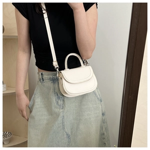 Detail of a creamy white leather saddle bag with gold-tone hardware and adjustable strap