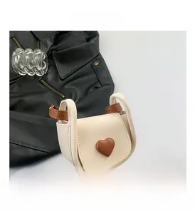Detail of a beige mini saddle bag featuring a brown heart ornament and thin shoulder strap