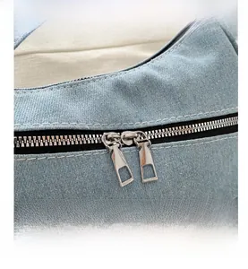 Detailed close-up of dual silver metal zippers on light blue denim shoulder bag