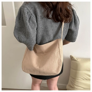 Detailed back view of a beige corduroy tote bag worn by a model in a cozy indoor setting