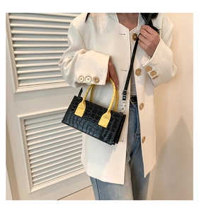 Detail of black faux crocodile texture handbag with contrasting yellow top handle