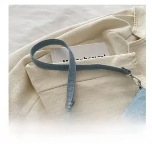 Detail of light blue denim handbag featuring white stitching and silver metal zipper hooks