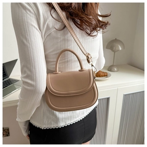 Beige PU leather saddle bag worn as a crossbody showing adjustable strap and top handle