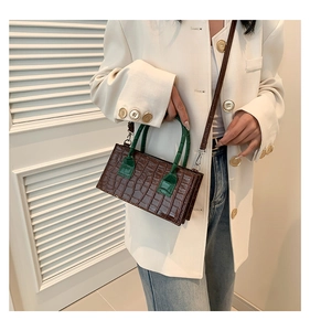 Detail of dark brown stone textured crossbody bag with green handle on white blazer