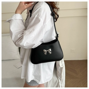 Detail of black crossbody bag featuring silver bow accent and knotted shoulder strap