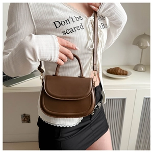 Brown semi-circular leather saddle bag with gold hardware shown in a cozy studio setting