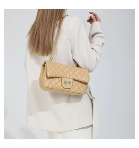 Detail view of beige quilted flap bag with gold chain strap on shoulder of cream blazer