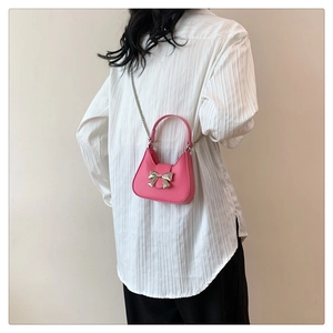 Pink mini crossbody bag featuring a silver metal bow and delicate chain shoulder strap