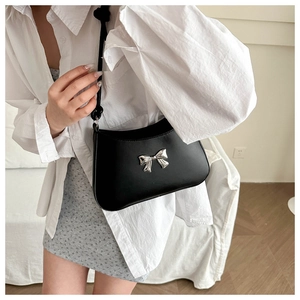 Detail of black leather underarm bag with silver bow accent shown on model