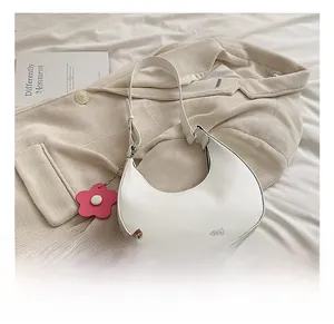 Close-up of white crescent shoulder bag with pink floral charm on beige corduroy