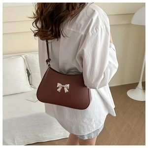 Detail of a brown leather shoulder bag with a silver metallic bow buckle on a model