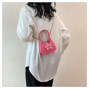 Detailed close-up of a pink mini crossbody bag with a silver metal bow and chain strap