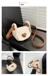 Detail of cream mini saddle bag featuring a brown heart ornament and leather shoulder strap
