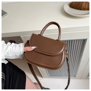 Detail of a dark brown mini saddle bag with a smooth PU leather finish and sturdy top handle