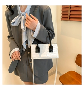 Detail of white crocodile pattern handbag with black handles and contrast trim details