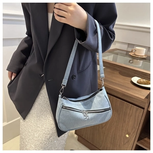 Borsa a mezzaluna in denim blu con cerniere metalliche indossata a spalla in un caffè