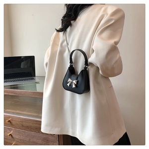 Mini black crossbody bag detail showing silver bow and chain strap on white blazer