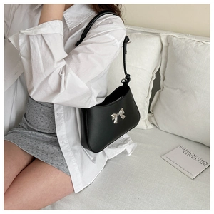 Detail of a minimalist black leather shoulder bag with a silver bow ornament