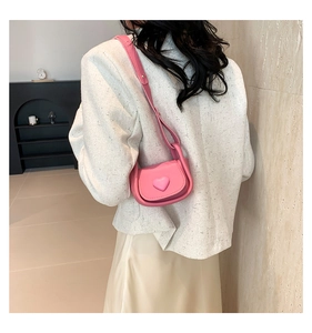 Detail of pink heart-shaped crossbody bag worn by a model in a modern indoor setting