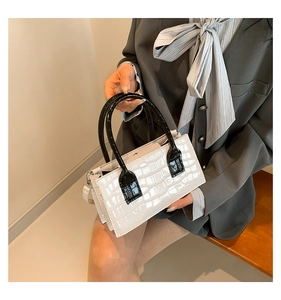 Detail of white crocodile pattern handbag with black handle and shoulder strap