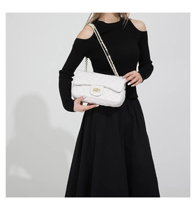 Close-up of white quilted chain bag with gold twist lock on black dress model