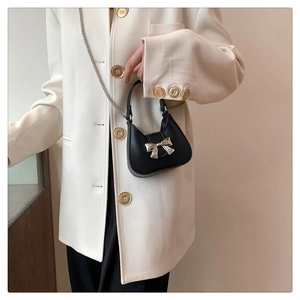 Detail of black mini crossbody bag featuring a metallic bow and silver chain strap