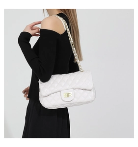 Detailed view of white quilted crossbody bag with gold chain strap on model