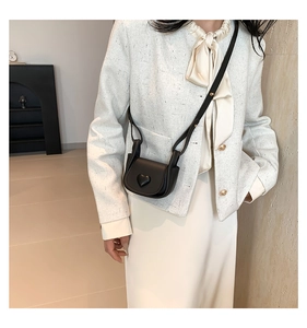 Close-up of black mini saddle bag with 3D heart detail on a white tweed jacket
