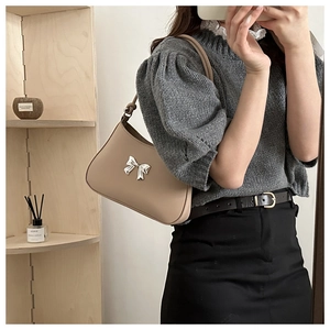 Detail shot of a beige faux leather underarm bag featuring a silver metal bow accent