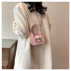 Pink mini PU leather handbag with silver metal bow and chain strap on a white blazer