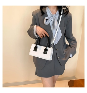 Detail of white crocodile texture handbag with black handle shown on grey suit model