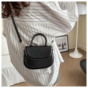 Detail of minimalist black leather saddle bag with gold metal hardware and crossbody strap