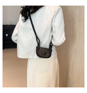 Close-up of a mini black saddle bag with heart detail worn with a tweed jacket