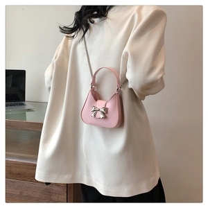 Detail of light pink mini bag with silver bow accent and elegant chain strap on a model