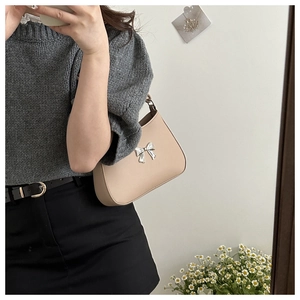 Detailed view of the silver metal bow accessory on beige faux leather shoulder bag