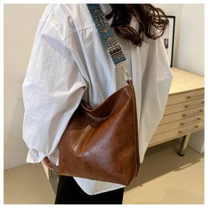 Close-up of brown leather tote bag featuring a colorful embroidered jacquard strap