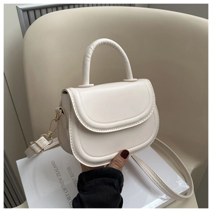 Detail of a creamy white mini saddle handbag with golden hardware on a minimal background