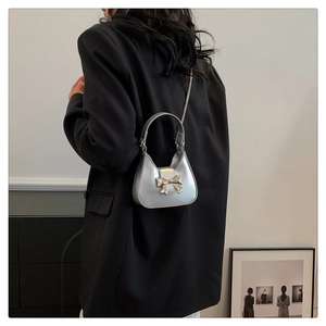 Silver metallic mini shoulder bag with bow detail worn by a model in a black suit
