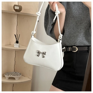 Detail of white shoulder bag featuring a silver metal bow and knotted strap design