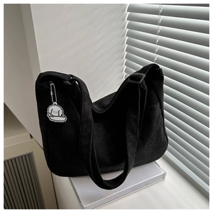 Detail of black corduroy tote bag showing vertical ribbed texture and white puppy charm