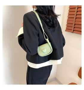 Detail of mint green mini saddle bag with heart ornament on black blazer