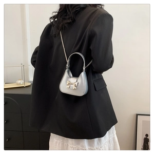 Close-up of a silver mini bow handbag worn over a black blazer for a stylish look