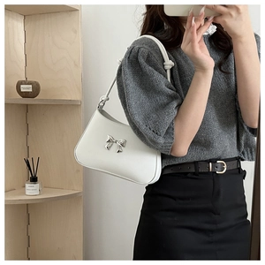 Detail of white faux leather shoulder bag with silver metal bow and twisted strap