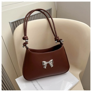 Detail of caramel leather handbag featuring a silver metal bow and knot handle design