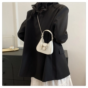 Detail of a creamy white mini handbag featuring a golden bow and chain on a model