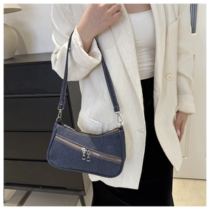 Dettaglio della borsa sottobraccio in denim blu con zip indossata da una modella
