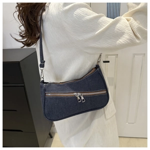 Dettaglio della borsa denim blu sottobraccio con cerniera argento su una modella